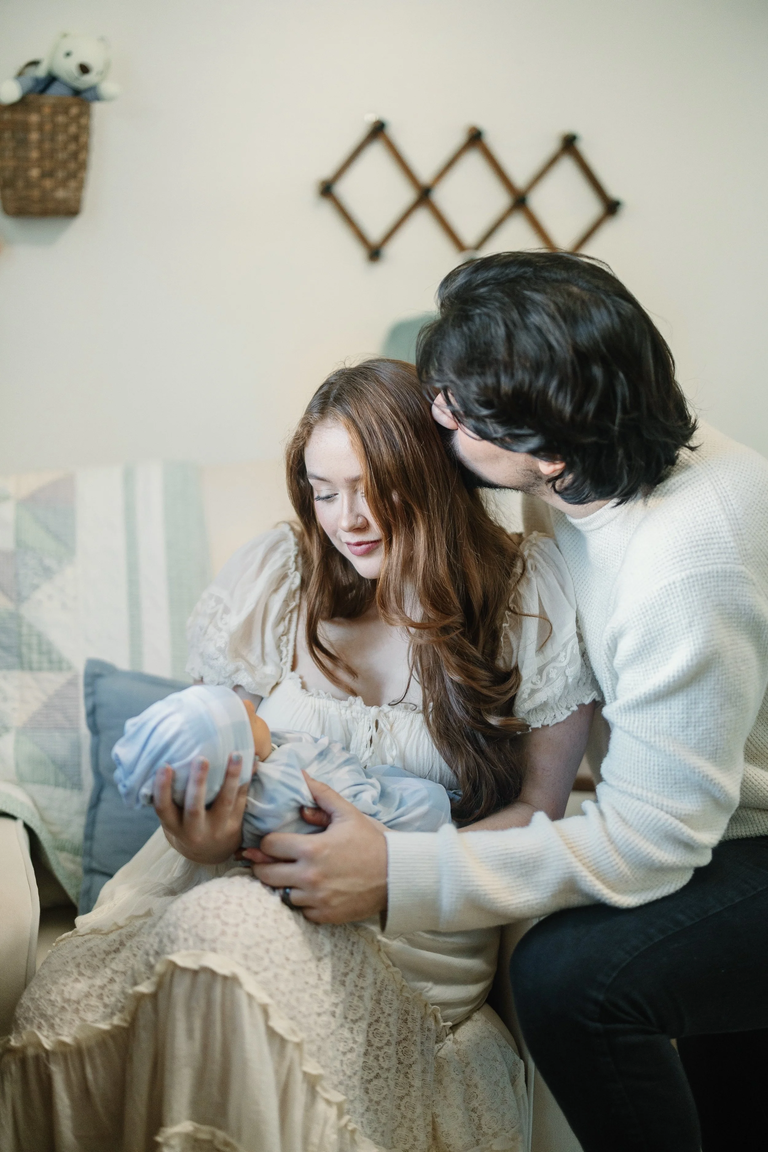 A woman holding a newborn baby, with a man leaning in close to her, in a cozy home setting.