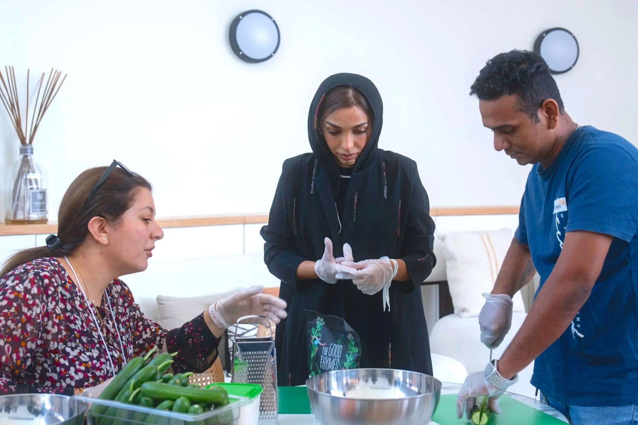 People conducting a nurse or medical training session, with a woman receiving treatment and two of them working on her arm, surrounded by medical supplies and equipment.