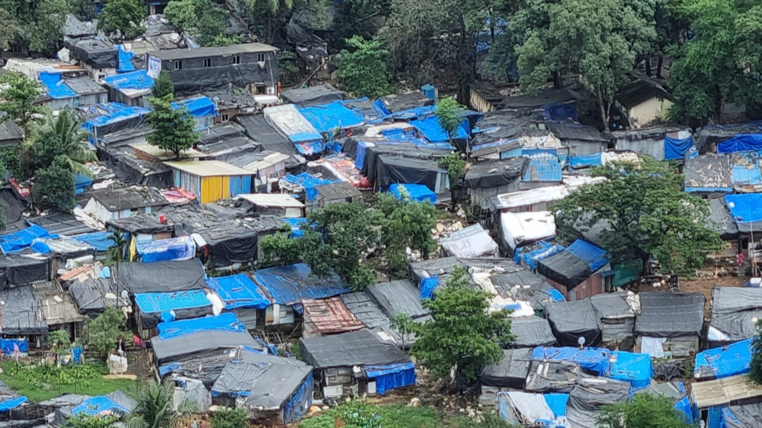 A view over the rooftops of an informal settlement. The roofs seem to be made of plastic sheeting and all the dwellings are very closely packed together