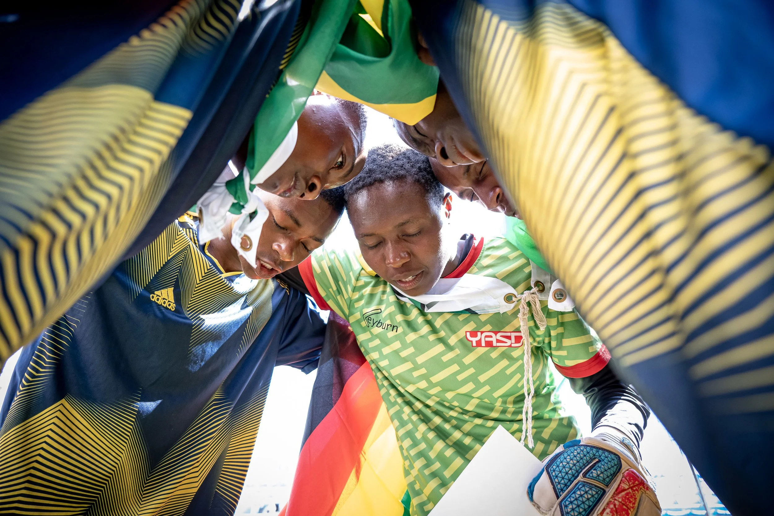 Five players stand together in a circle looking down with their eyes closed wearing Zimbabwean national kit