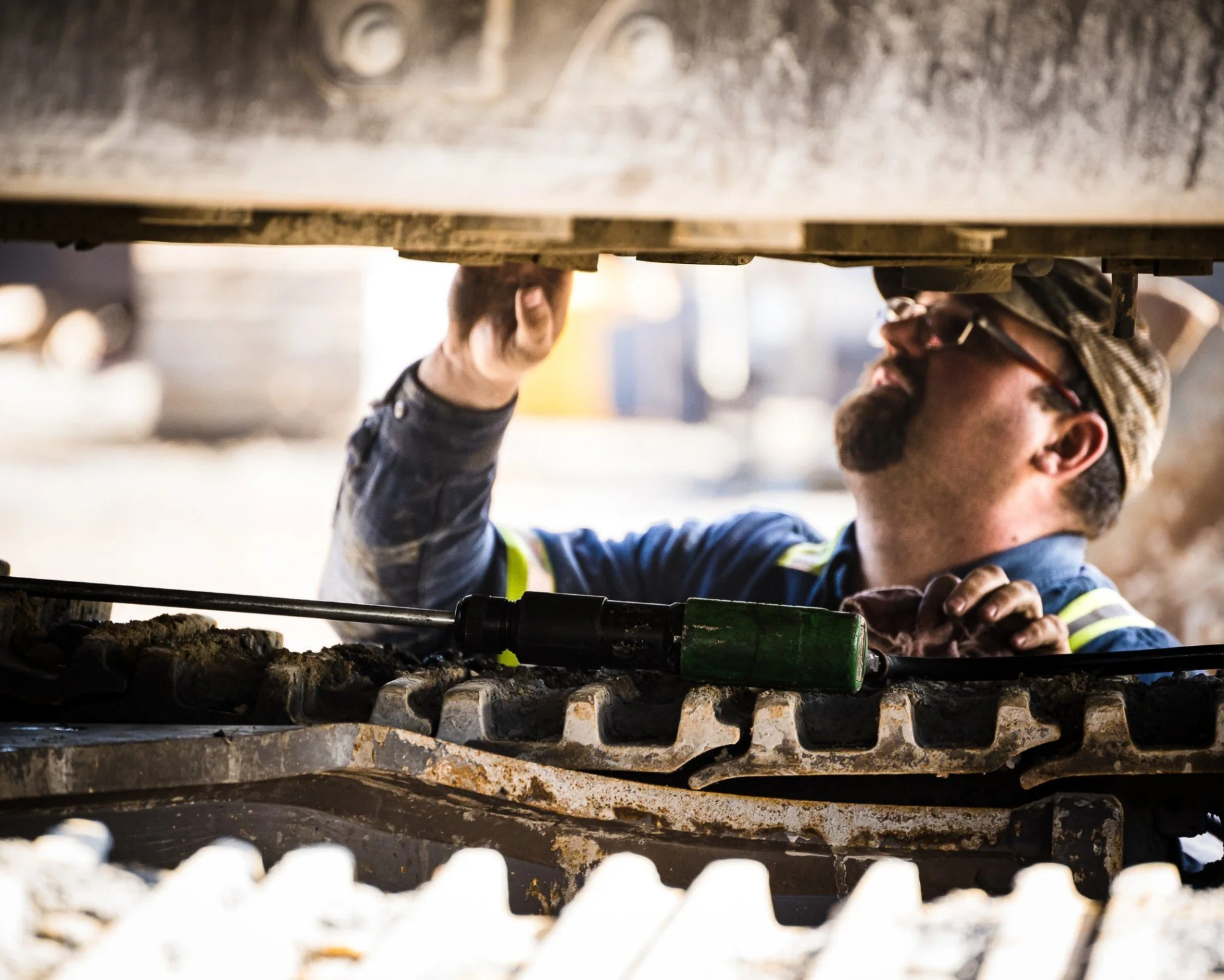 Construction worker performing maintenance beneath heavy equipment on an active jobsite