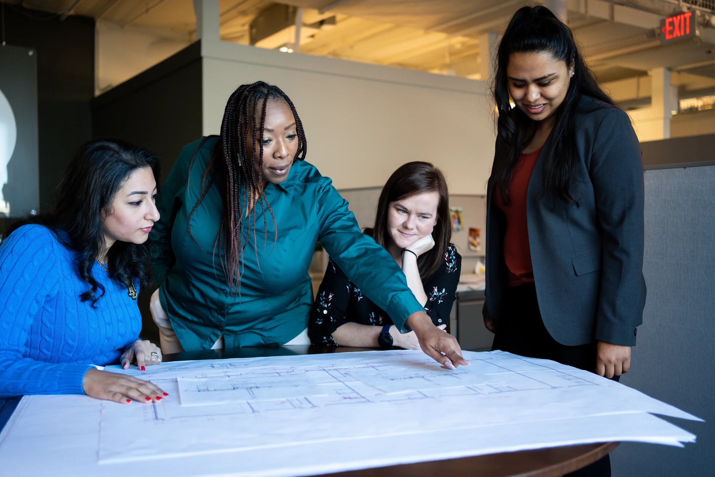 Four professional women collaborating over architectural blueprints in a modern office