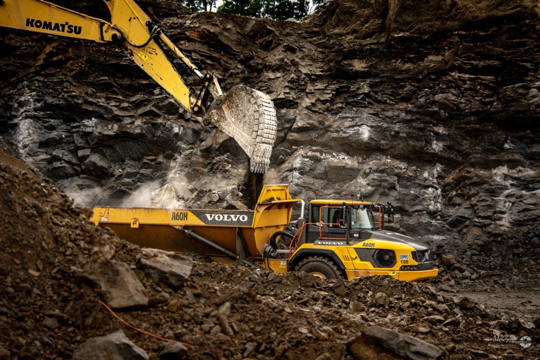 Excavator loading rock into a haul truck inside an active quarry construction site