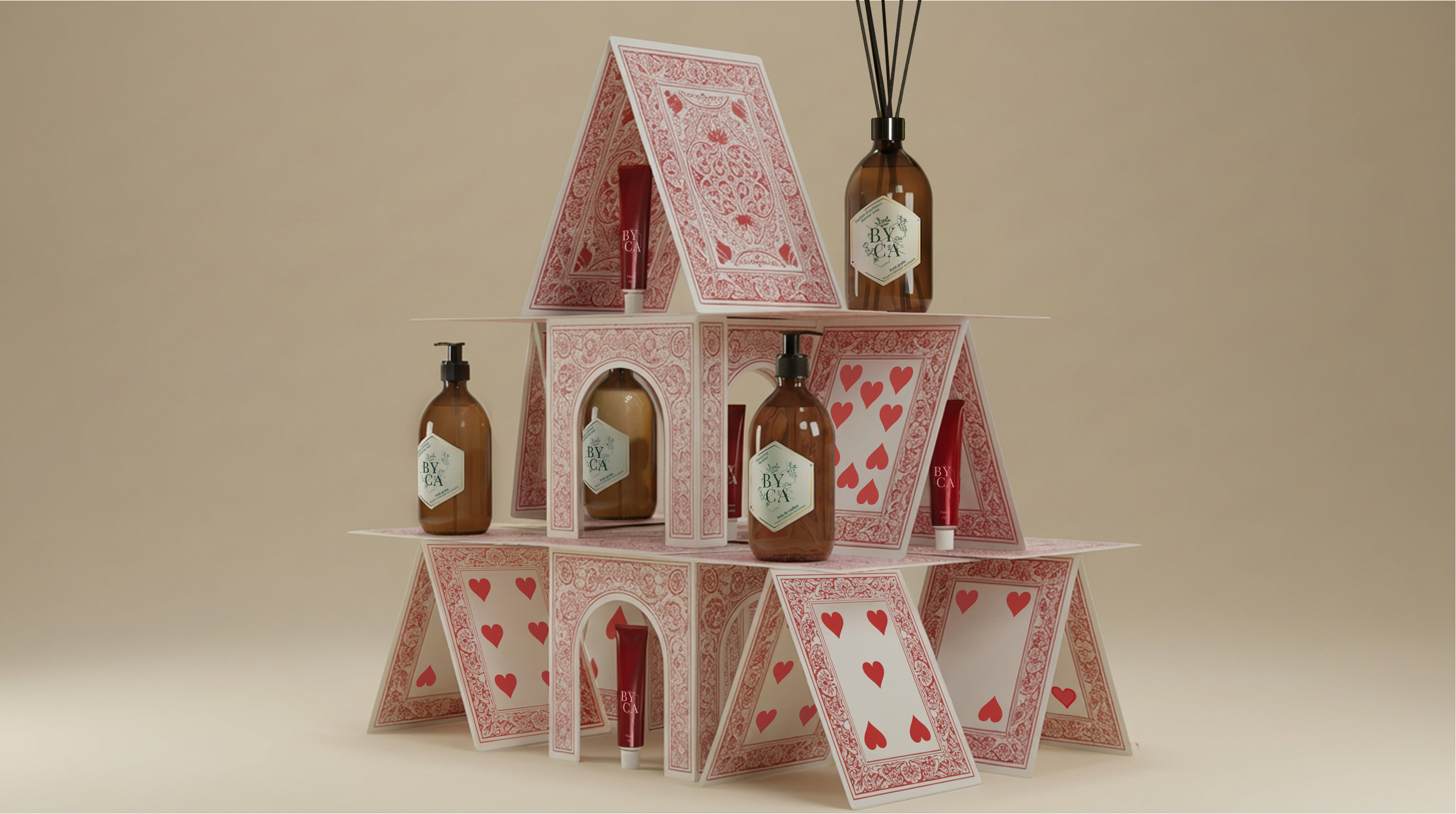 Un pyramid de cartes à jouer rouges et blanches avec des bouteilles en verre marron et des tubes de crème rouge, toutes portant une étiquette avec écrit « BY CA ».