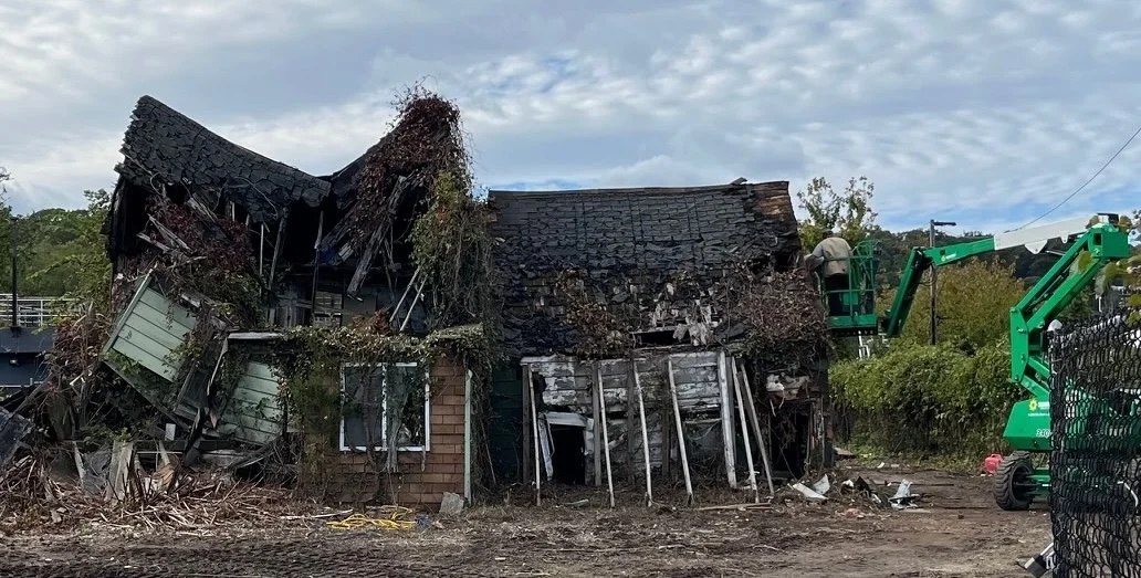 A collapsing house with a worker working from a green hydraulic crane