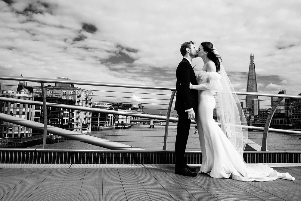 Bride and groom walking across Millennium Bridge with St Paul's Cathedral and the Shard in the background &mdash; iconic London wedding photography by Oliver Holder