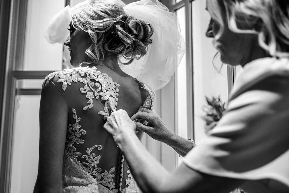 The back of Katie&rsquo;s lace wedding dress being fastened before the ceremony