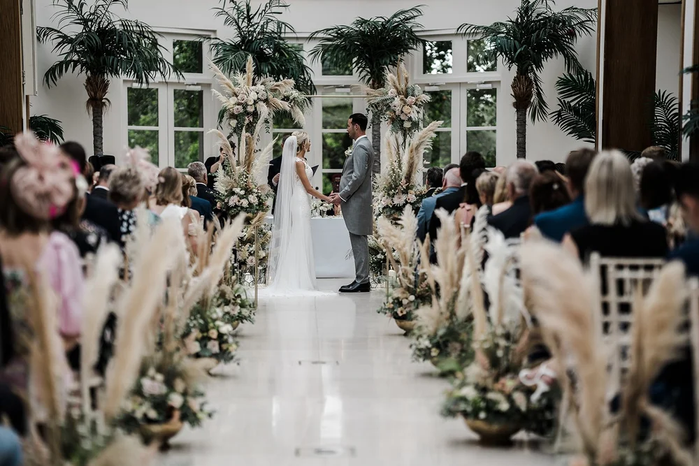 Katie walking down the aisle of the Palm Court at The Hurlingham Club