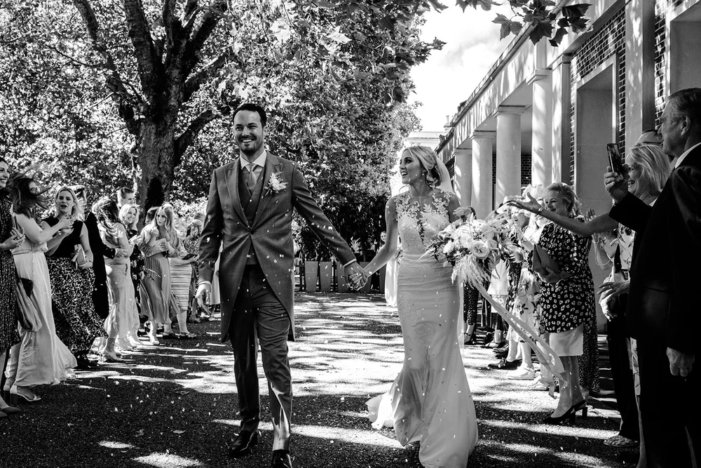 Black and white photograph of Mike and Katie in the confetti line at The Hurlingham Club