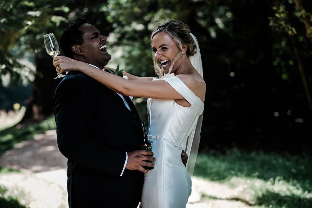 Bernie and Naesan laughing with champagne in the gardens at Grantley Hall