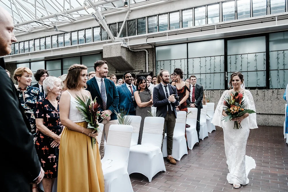 Anna walking down the aisle towards Jordan in the Barbican Conservatory