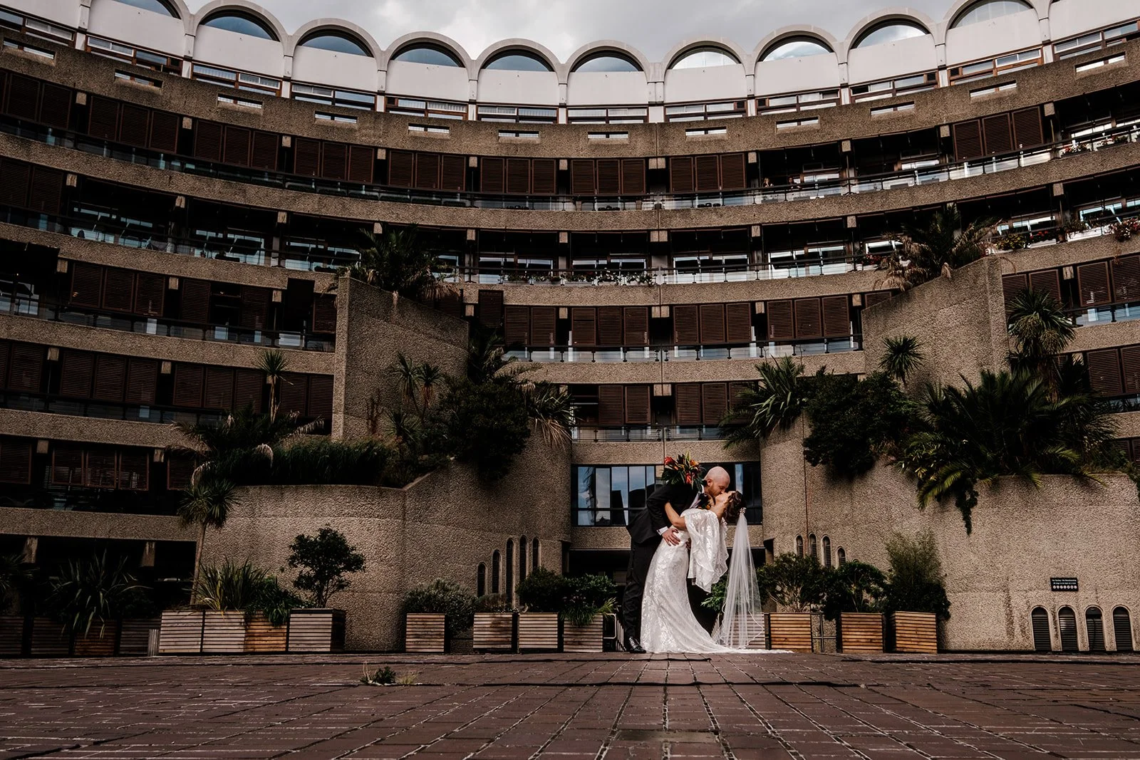 Jordan and Anna dwarfed by the curved concrete balconies of the Barbican, photographed from across the terrace