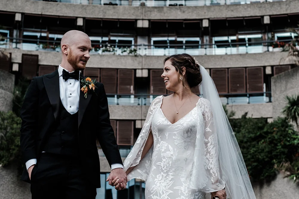 Jordan and Anna holding hands beneath the curved concrete of the Barbican