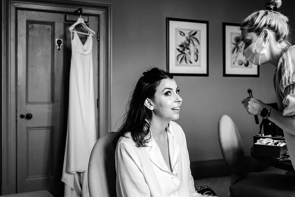 Sarah getting ready on the morning of her Clevedon Hall wedding, the dress hanging behind her