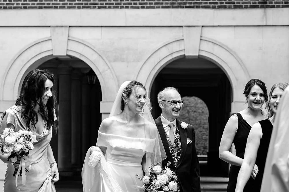 Black and white photograph of Gina arriving with her father and bridesmaids at Temple Church