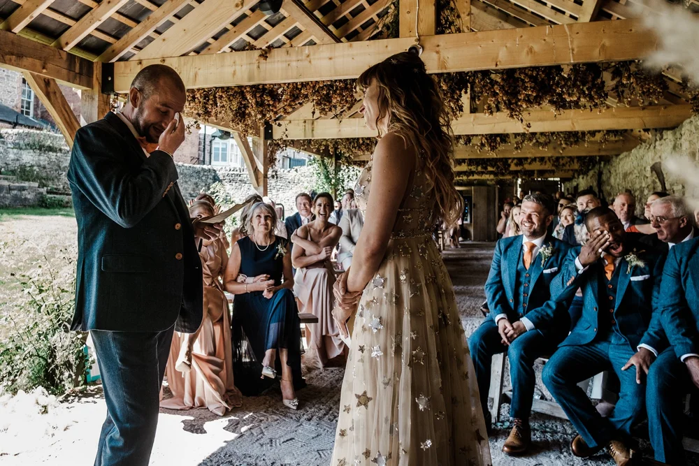 Jess and Tom facing each other during the ceremony in the barn at Lyde Court