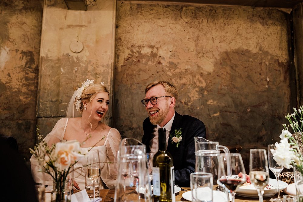 Guests reacting to the wedding speeches against the bare plaster walls at Wilton&rsquo;s Music Hall