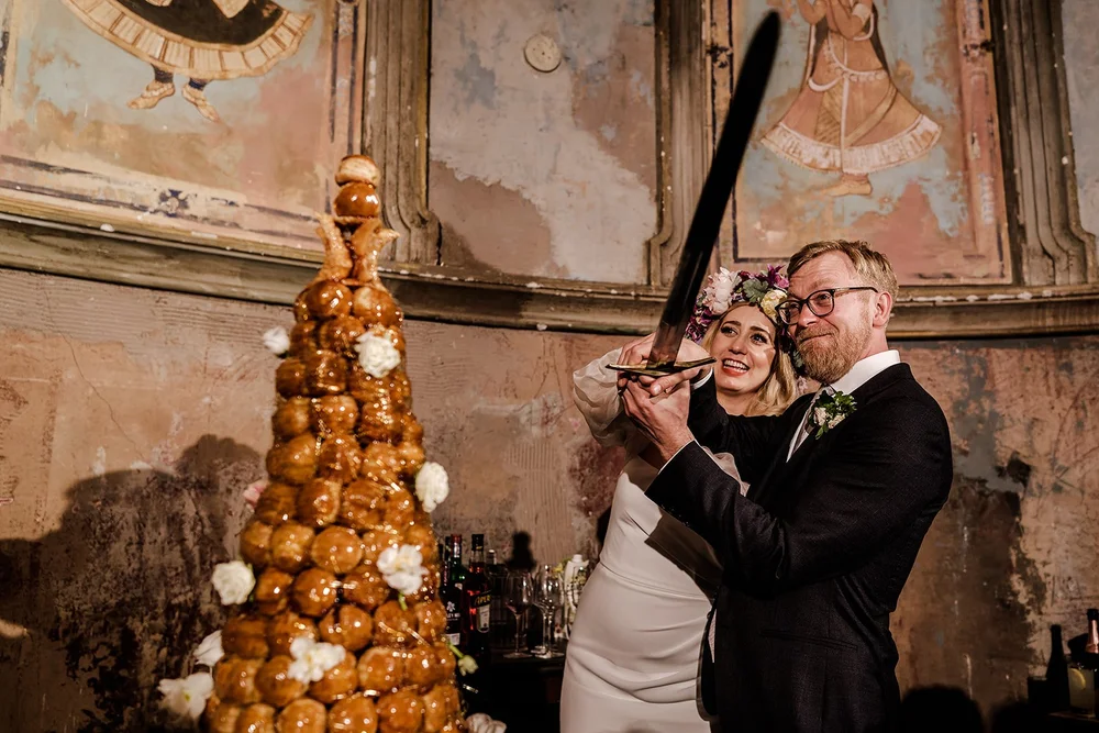 Meg and Jamie cutting the croquembouche with a sabre at Wilton&rsquo;s Music Hall