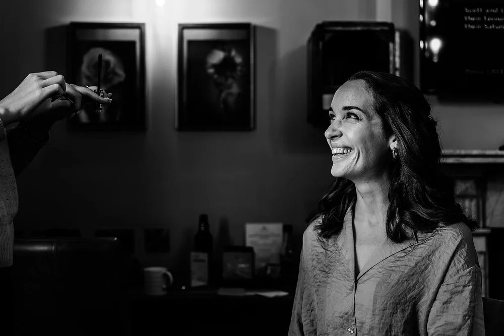 Black and white photograph of Charlotte having her make-up done before her London wedding