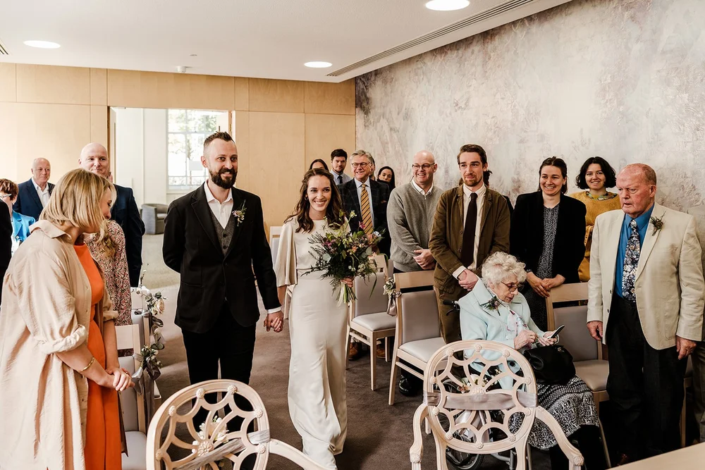 Charlotte walking into the ceremony room at Lambeth Town Hall with her guests standing