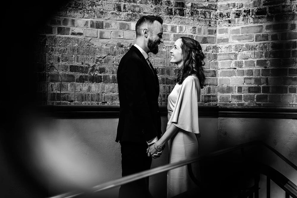 Black and white photograph of Aidan and Charlotte against exposed brickwork