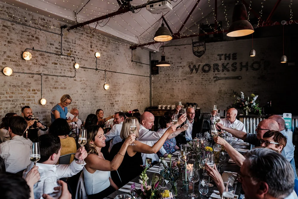 Guests raising a toast under festoon lights at The Workshop at the Half Moon