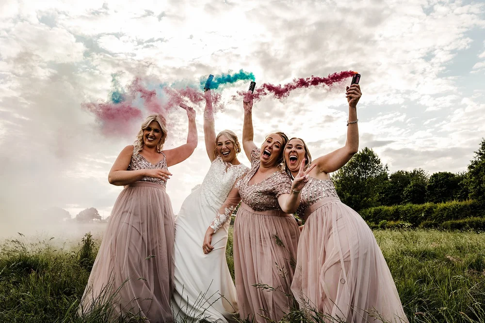 Lauren and her bridesmaids with coloured smoke grenades in the field at Willow Marsh Farm