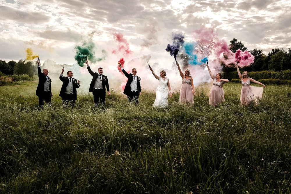 The whole wedding party with coloured smoke grenades in the meadow at Willow Marsh Farm