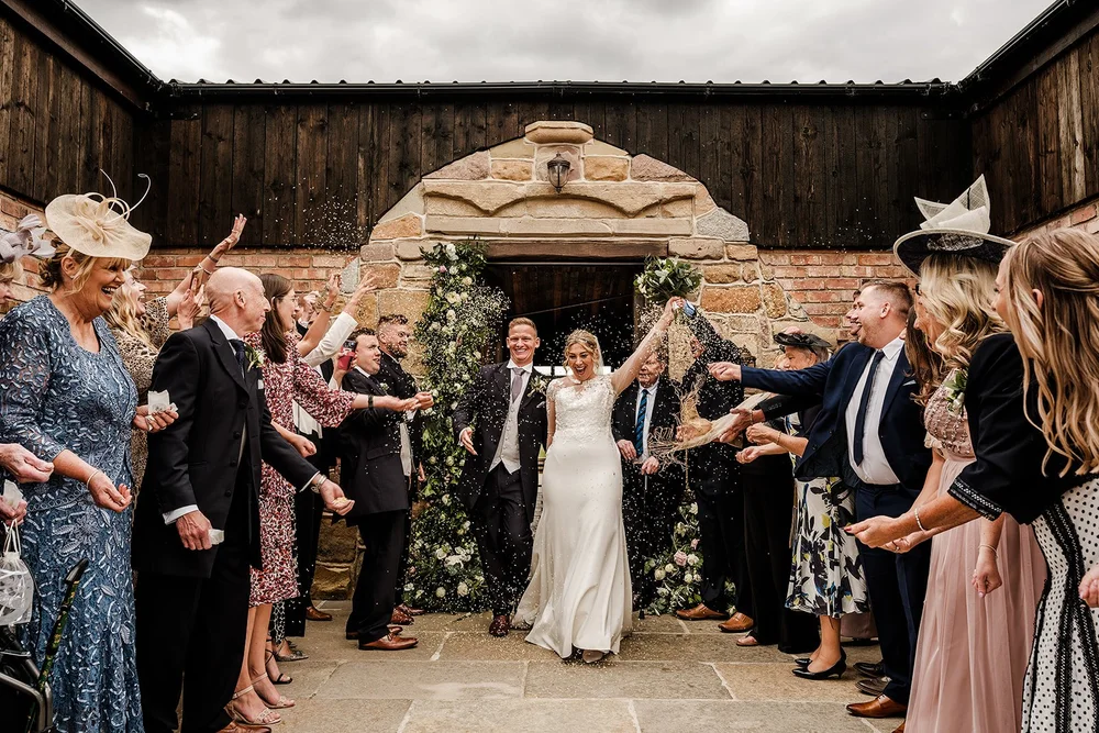 Lauren and Tom walking through a confetti tunnel of guests at Willow Marsh Farm