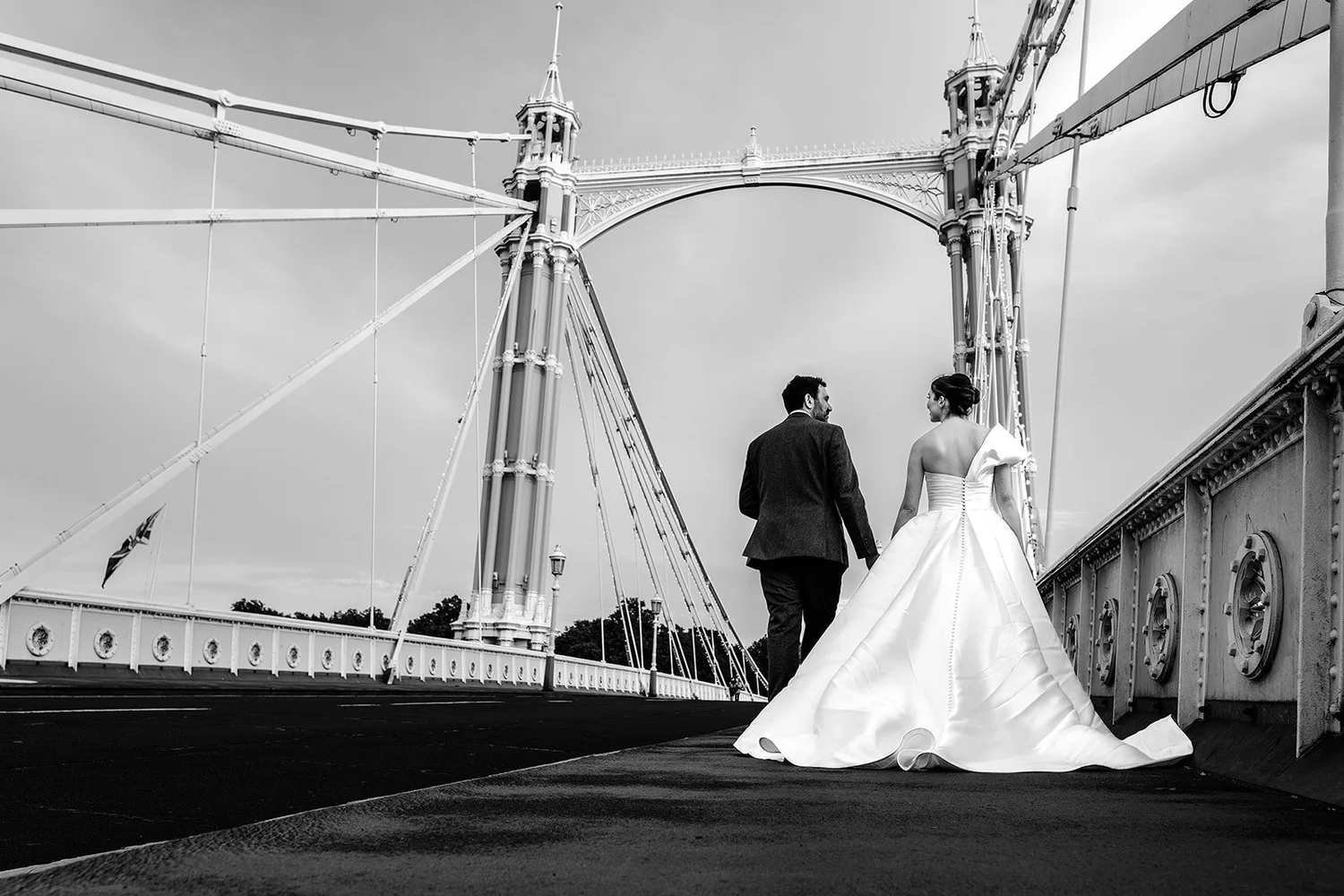 Black and white portrait of a bride and groom crossing Albert Bridge in Chelsea