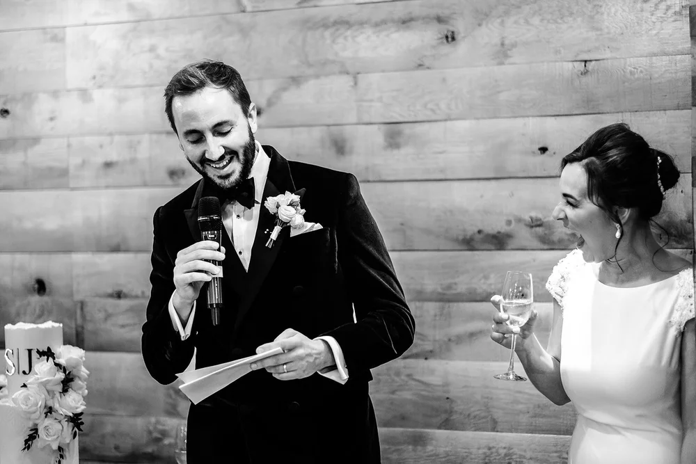 Black and white photograph of the couple laughing during the speeches