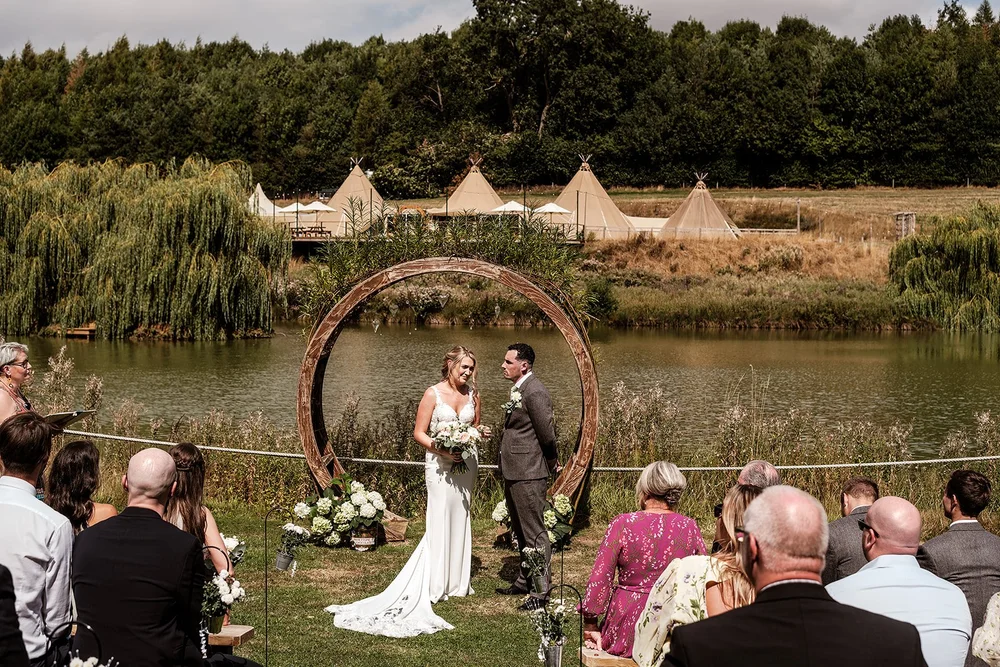 The outdoor ceremony beside the lake at Hadsham Farm under a circular floral arch