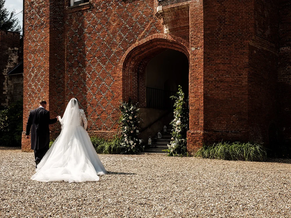 Jade walking towards the gatehouse arch at Farnham Castle in her wedding dress