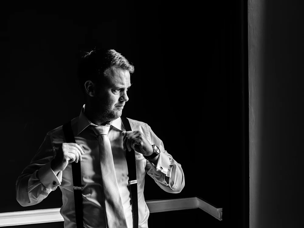 Black and white photograph of Guy fastening his tie before the ceremony