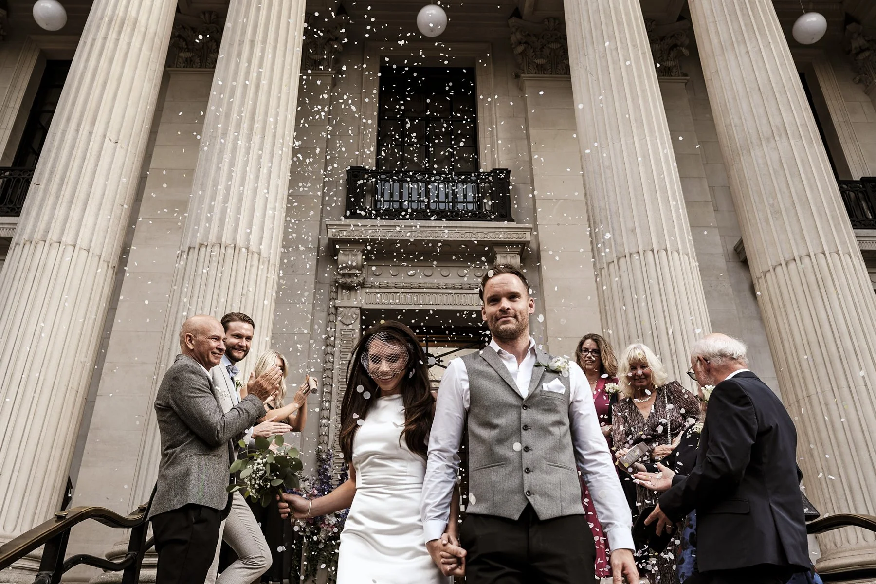 A newly married couple walking out between the columns of Old Marylebone Town Hall in a shower of confetti