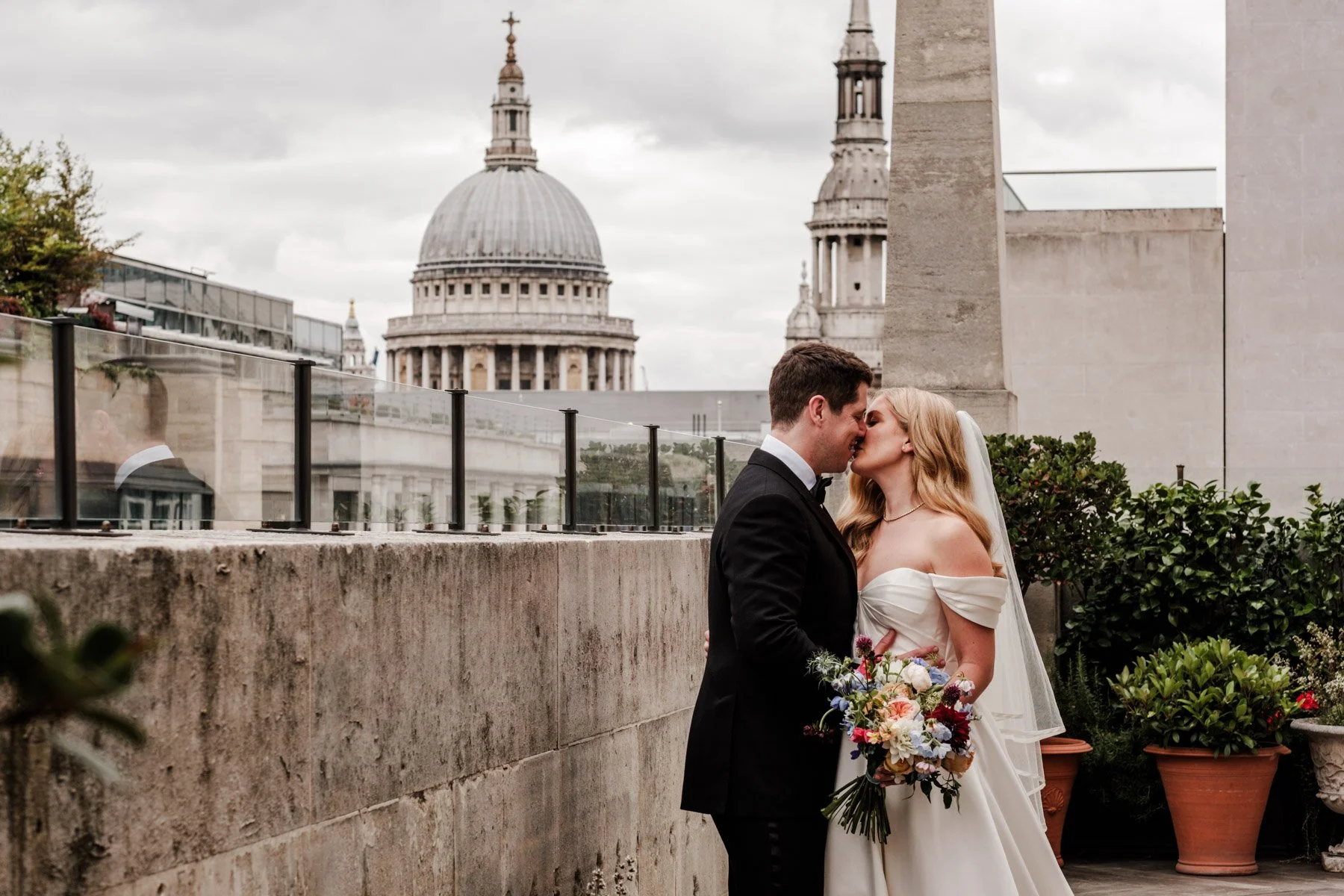 Bride and groom kiss on the roof terrace at The Ned Hotel, with St Paul's Cathedral rising behind them in the London skyline