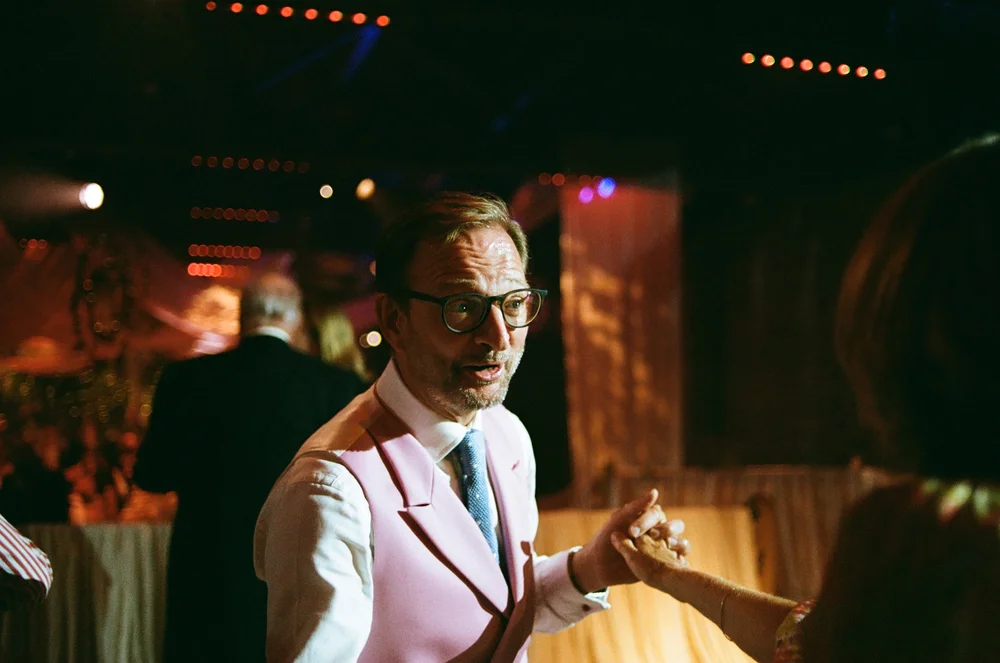 A wedding guest under festoon lights in the evening, shot on 35mm colour film