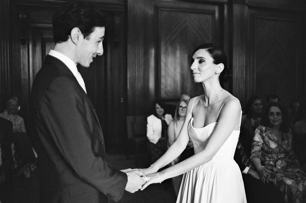 Bride and groom holding hands during their wedding ceremony, photographed on 35mm black and white film