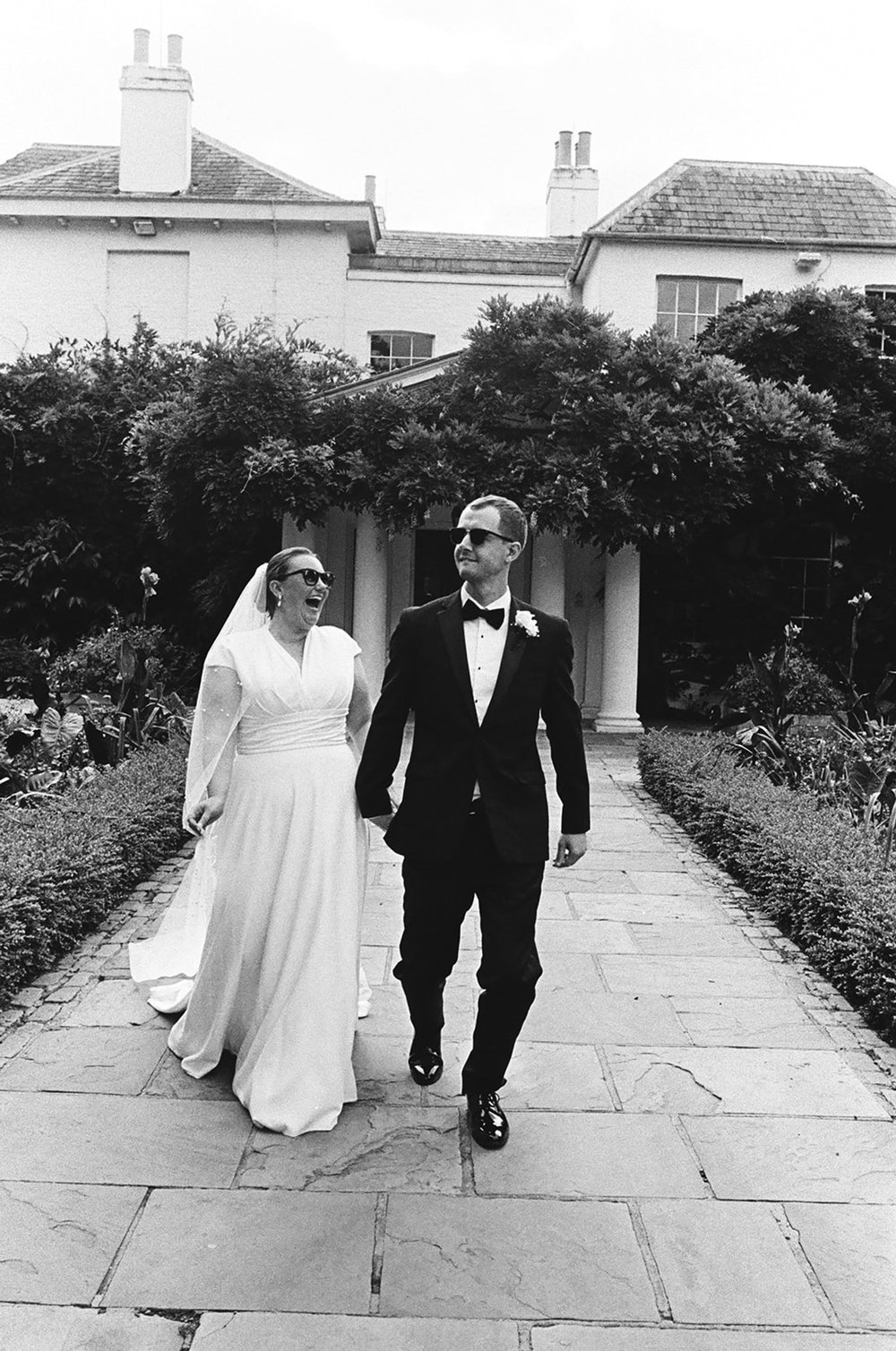 Bride and groom walking down a garden path together, photographed on 35mm black and white film