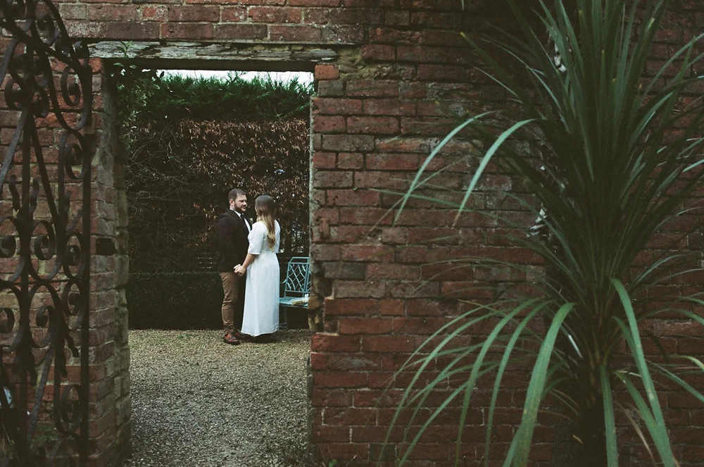 Bride framed in a walled garden doorway, photographed on 35mm film