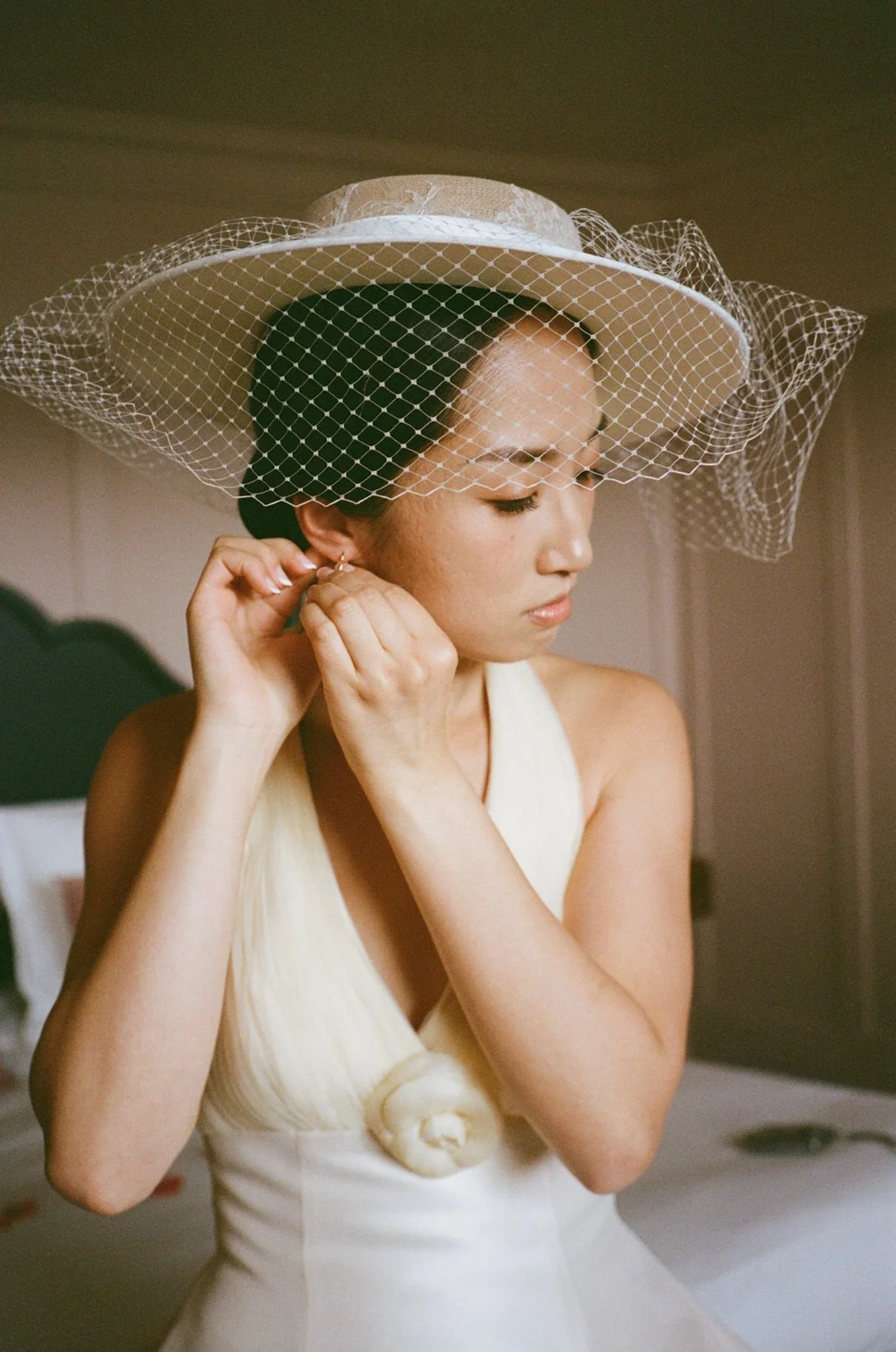 Bride in a birdcage veil putting in her earrings, photographed on Kodak Portra 400