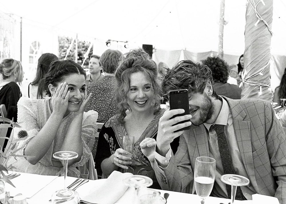 Wedding guests laughing together at the table, shot on 35mm black and white film