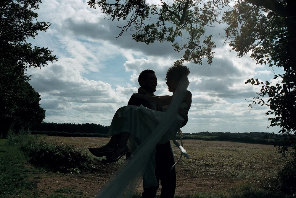 Bride and groom silhouetted against a wide sky, shot on 35mm film