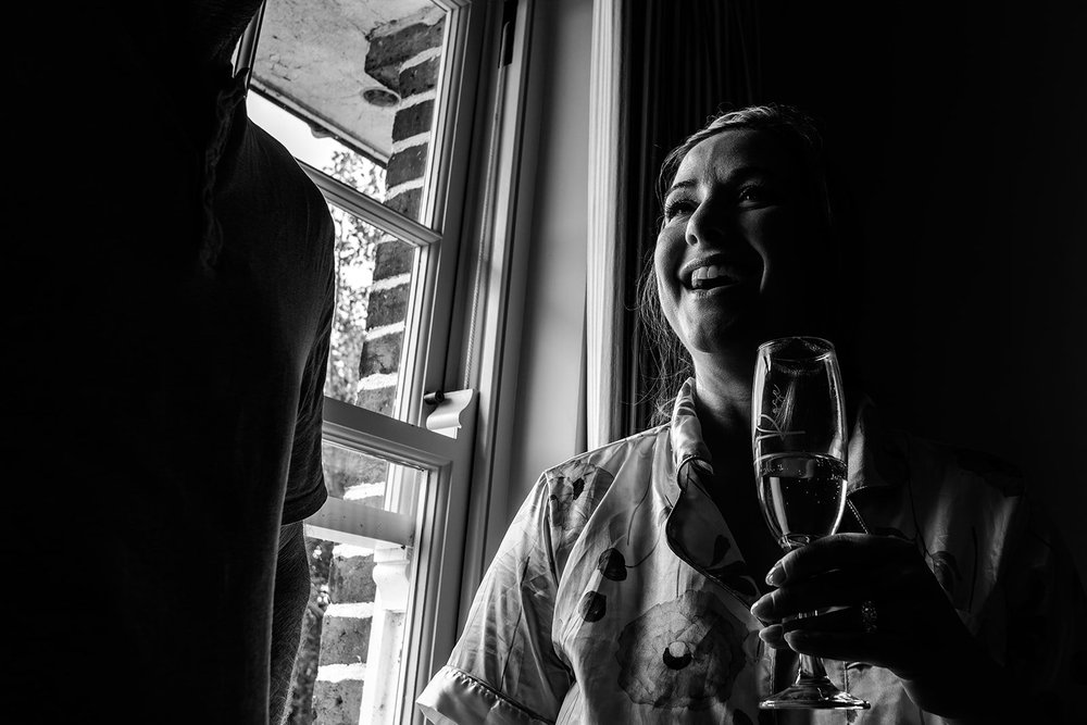 Rose with a glass of champagne by the window on her wedding morning at Elmley