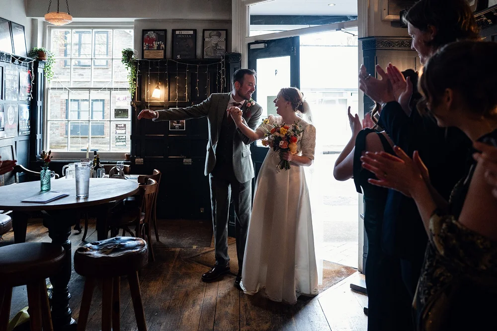 Ffion and Tom walking into the Alma Tavern to applause from their guests