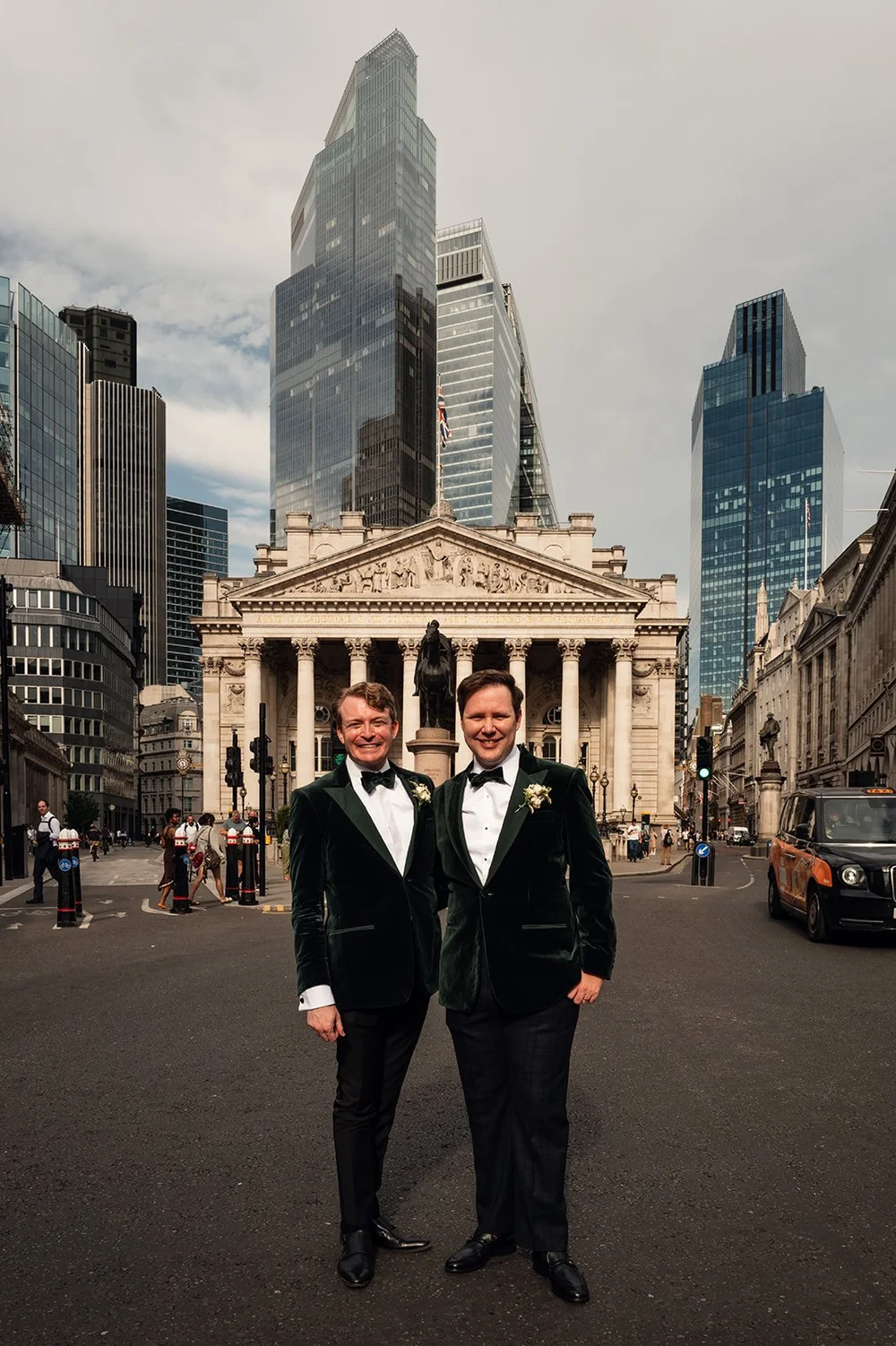 Two grooms outside The Ned with the Royal Exchange and the City of London skyline behind them