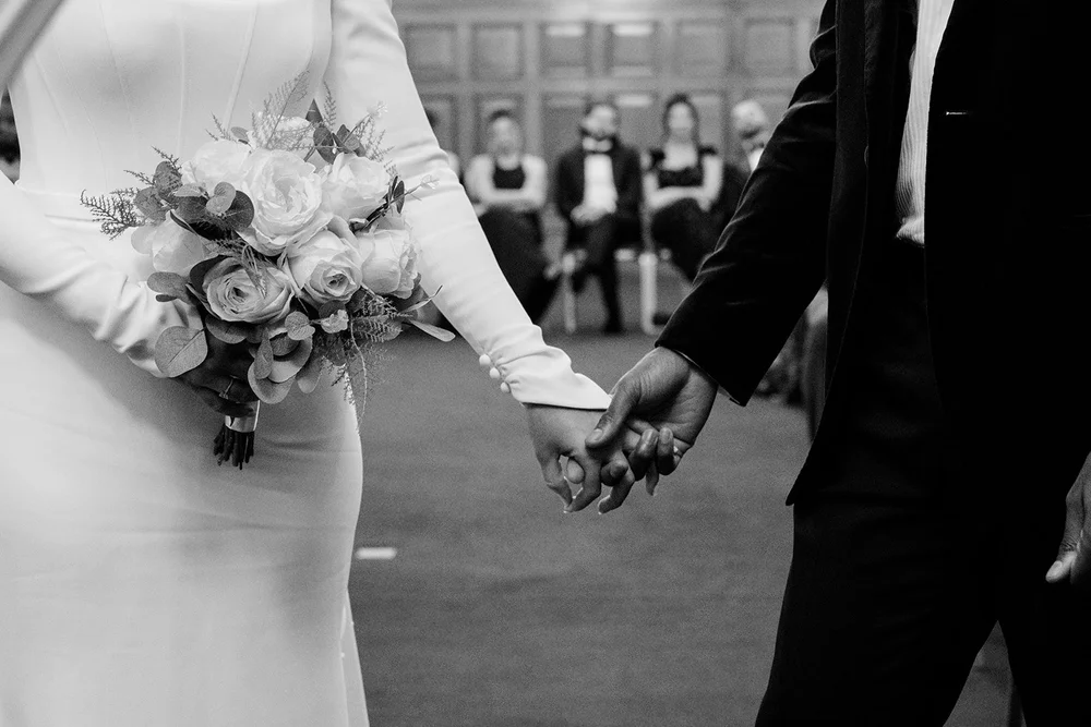 Black and white photograph of Sophie and Dan holding hands during their ceremony