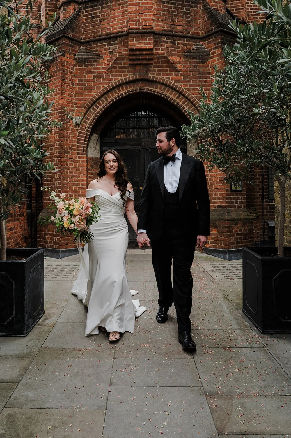 Chloe and Jon walking out through the brick archway at St Mary&rsquo;s Bourne Street