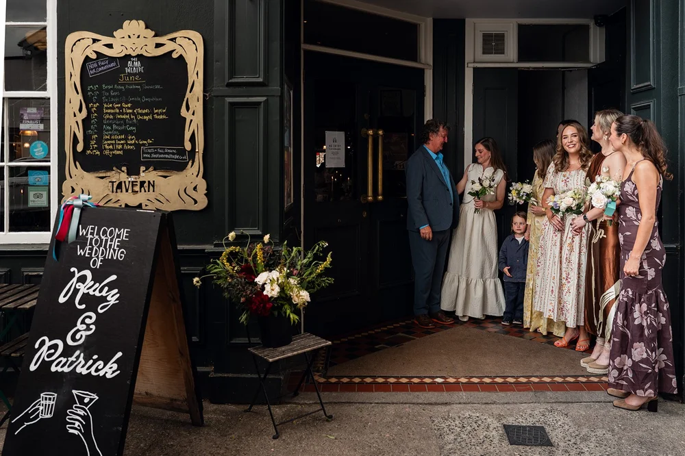 Guests arriving beside the welcome chalkboard at The Alma Tavern