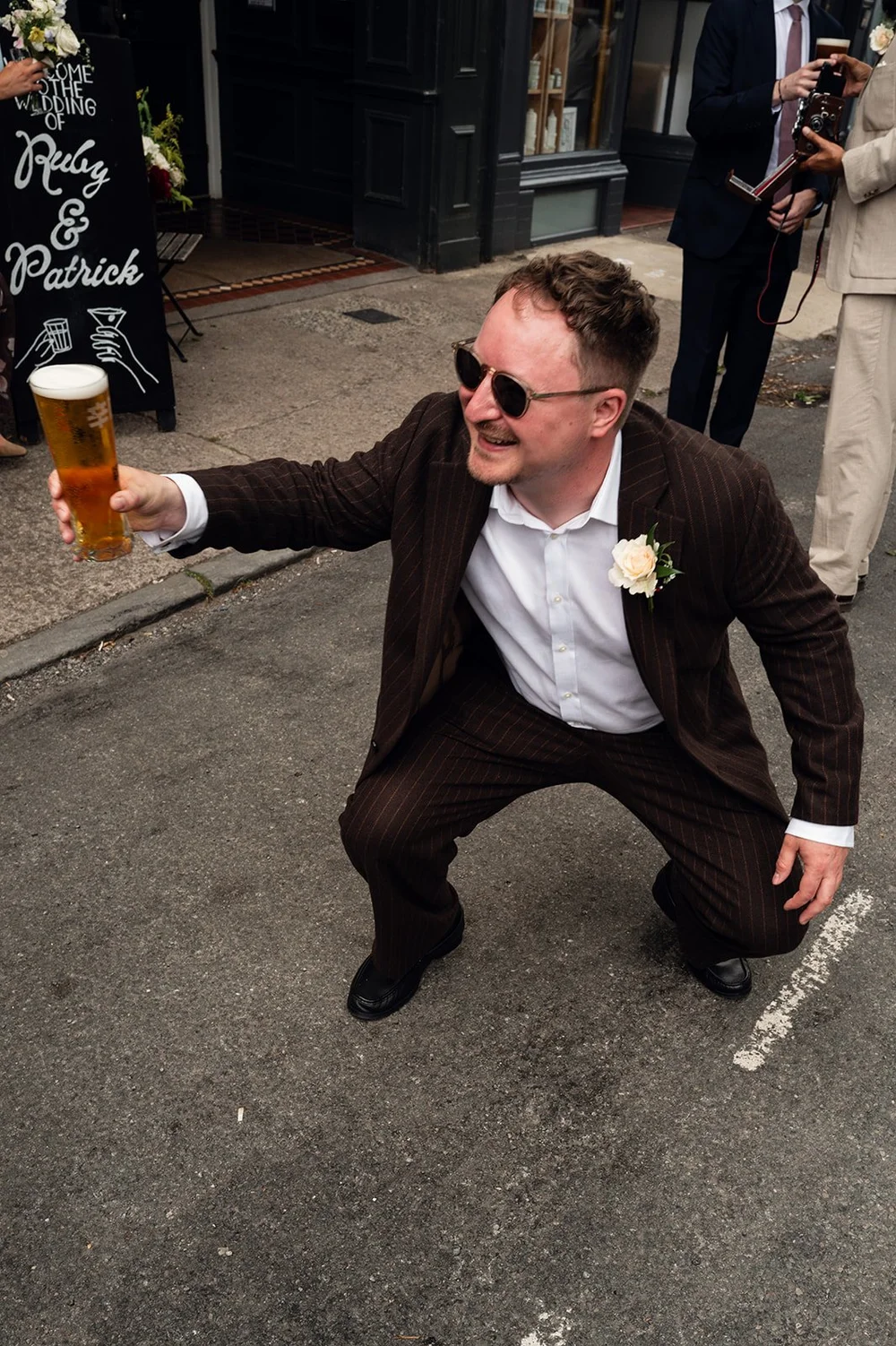 A guest crouching with a pint on the street outside the pub